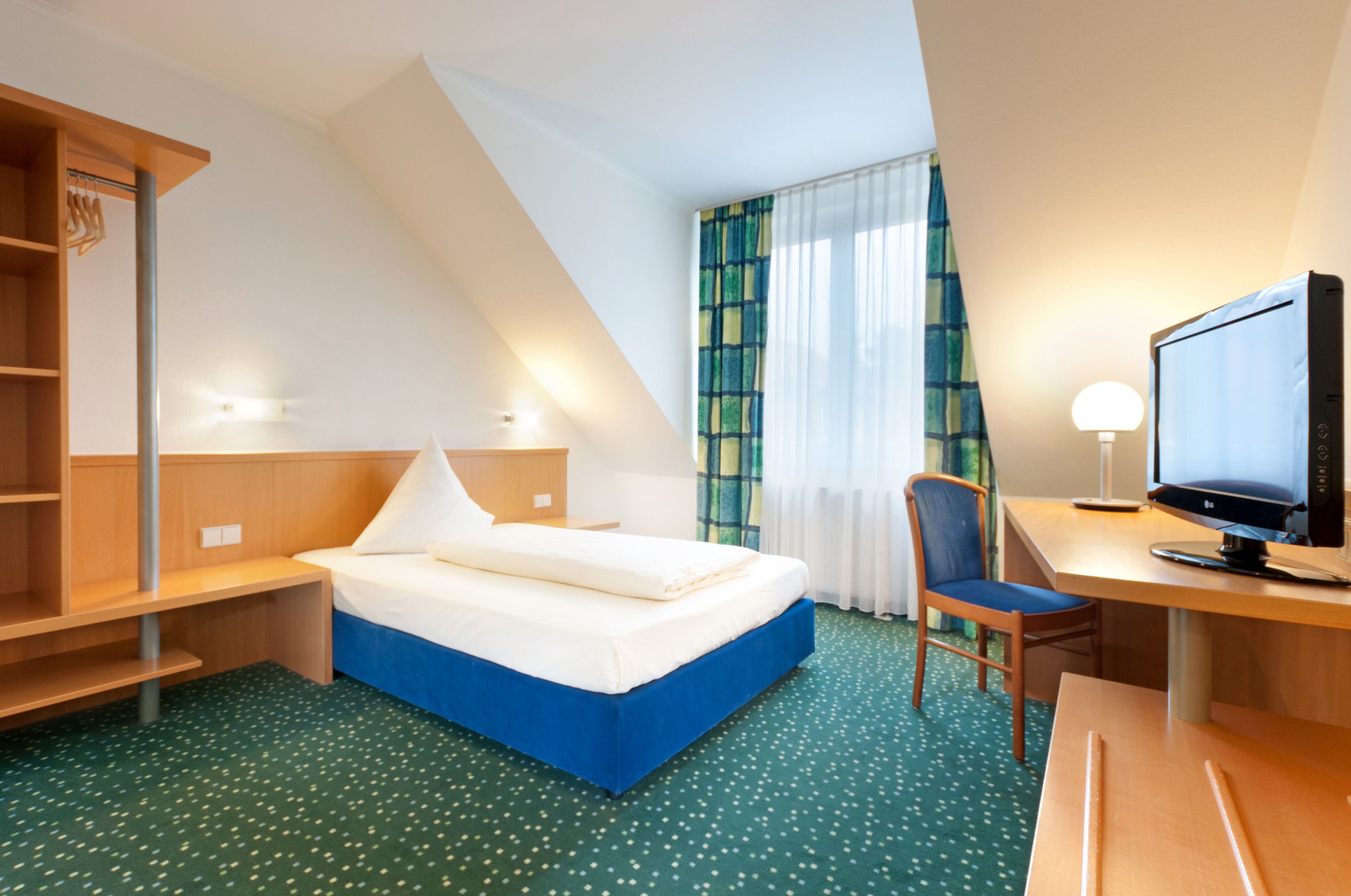 Hotellihuone, jossa on sänky, työpöytä, tuoli, televisio ja ikkuna, jossa on verhot.