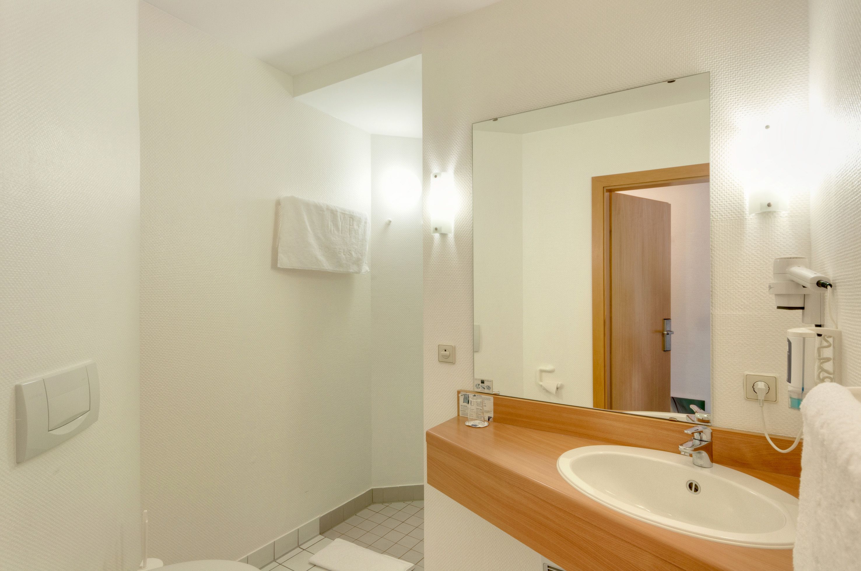A bathroom with a wooden vanity, a large mirror, and a white towel hanging on the wall.