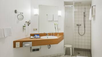 A modern bathroom with a wooden vanity, a sink, a mirror, a shower, and a small stool.