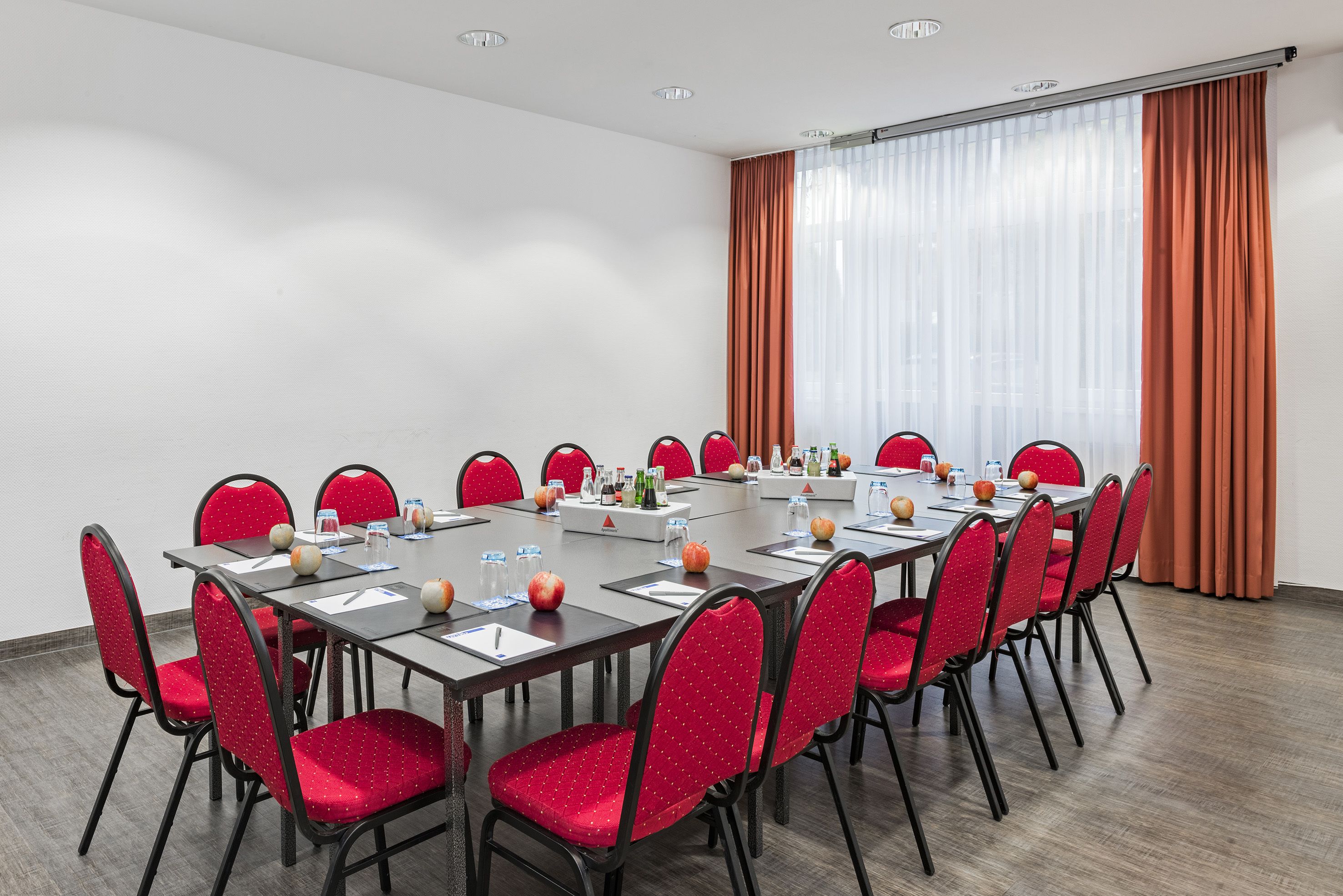 A conference room with a long table, red chairs, and a large window with curtains.