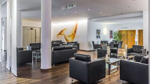 A modern lobby with dark leather sofas, a glass coffee table, and a large abstract wall art piece. - Hesse Hotel Celle (Celle)