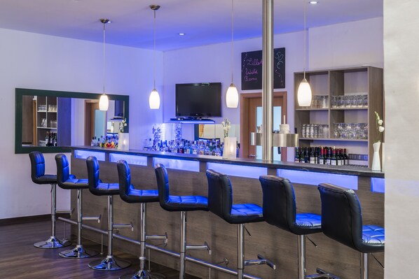 A bar area with multiple stools, a television, and shelves with bottles and glasses.