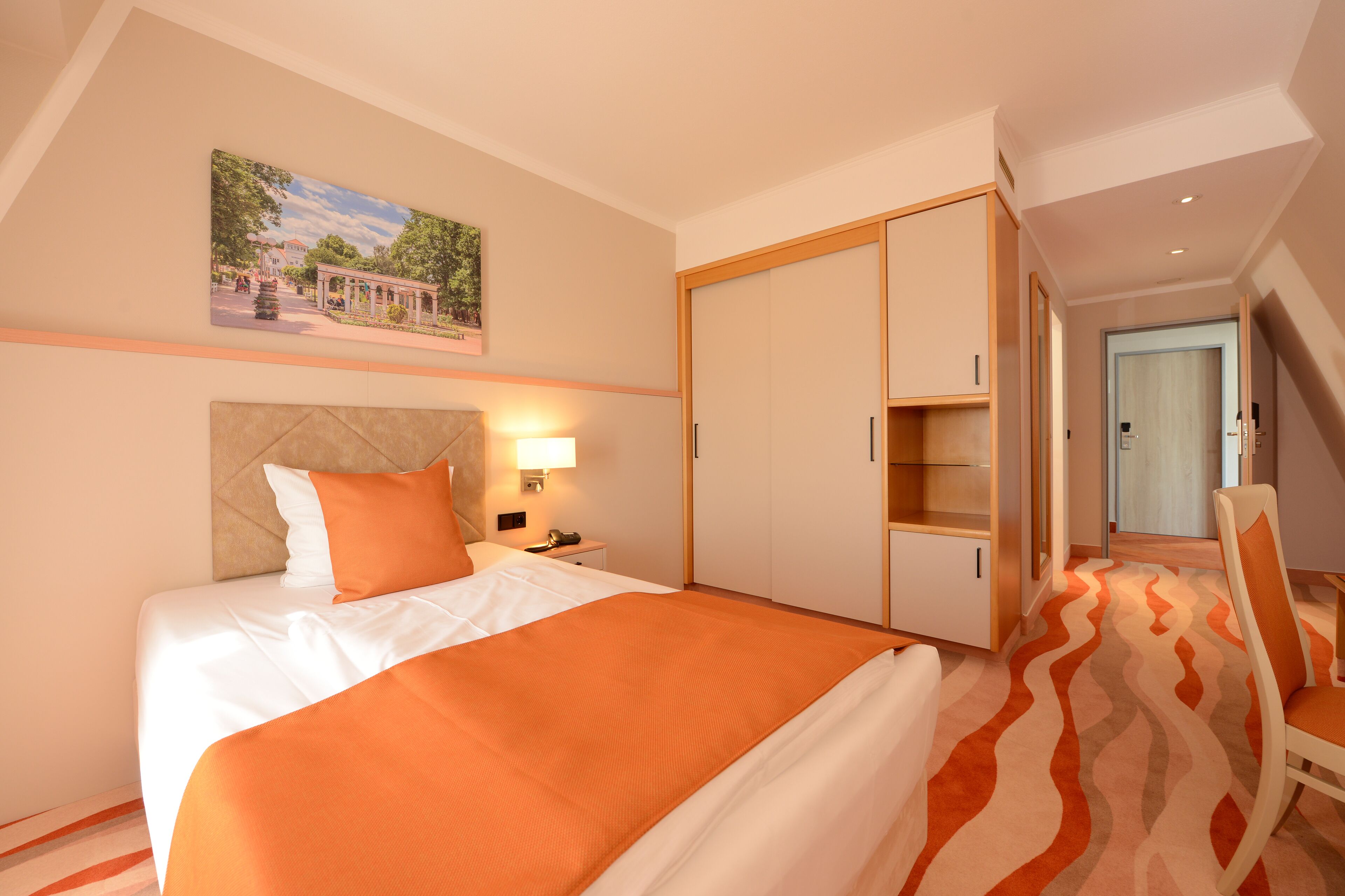 A hotel room with a bed, a nightstand, a lamp, a wardrobe, and a chair.