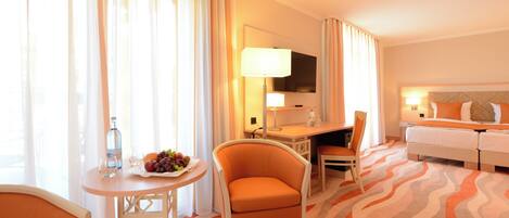 Habitación de hotel con cama, escritorio con silla, una mesita con otra silla y televisor en la pared.
