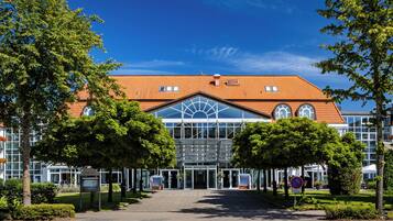 A modern hotel with a glass facade, a red-tiled roof, and a symmetrical entrance.