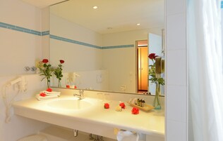 Ein Badezimmer mit einem großen Spiegel, einem weißen Waschbecken und zwei roten Rosen auf der Ablagefläche.