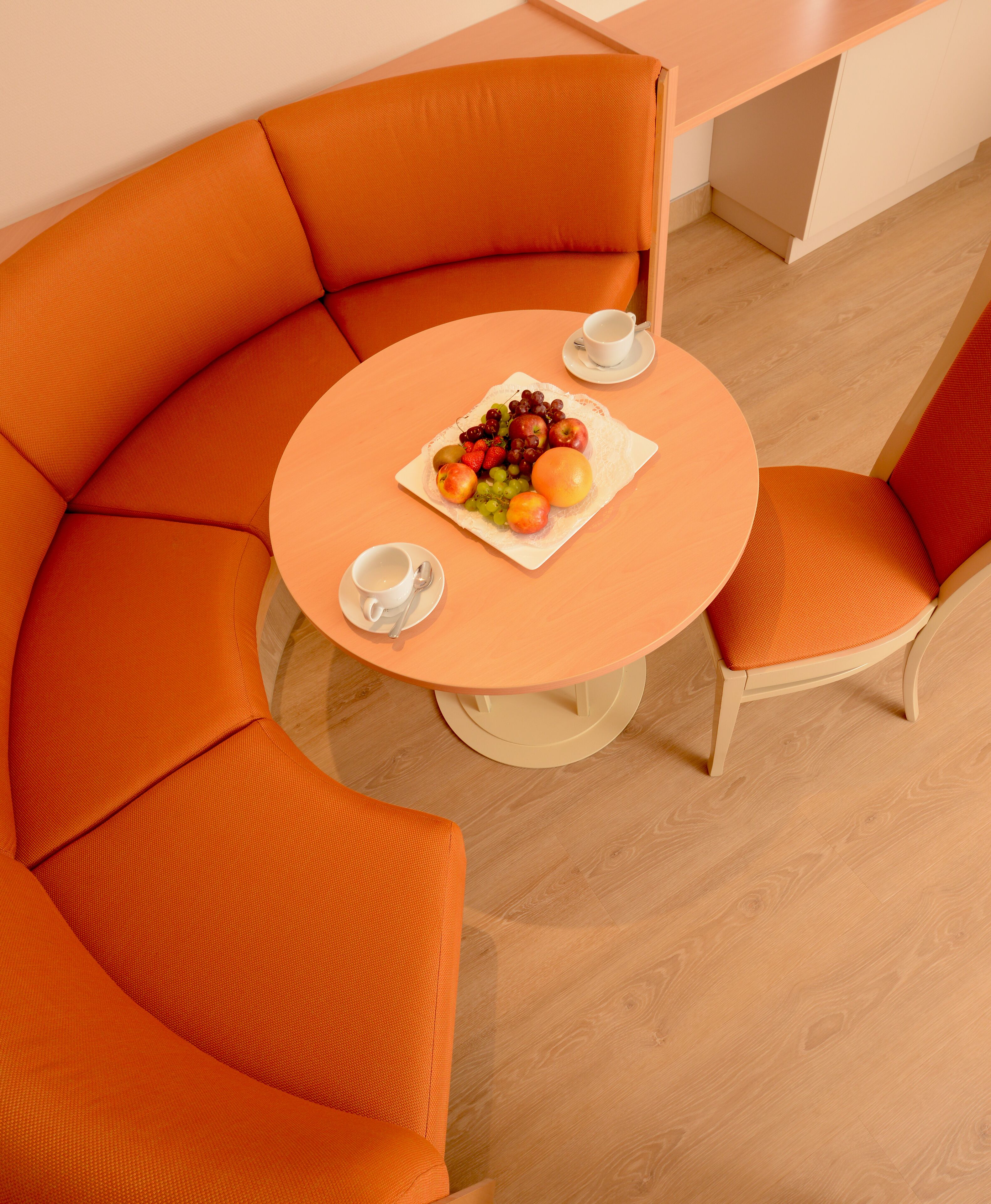 Ein moderner, orangefarbener Sitzbereich mit rundem Tisch, zwei Stühlen und einer Obstplatte.