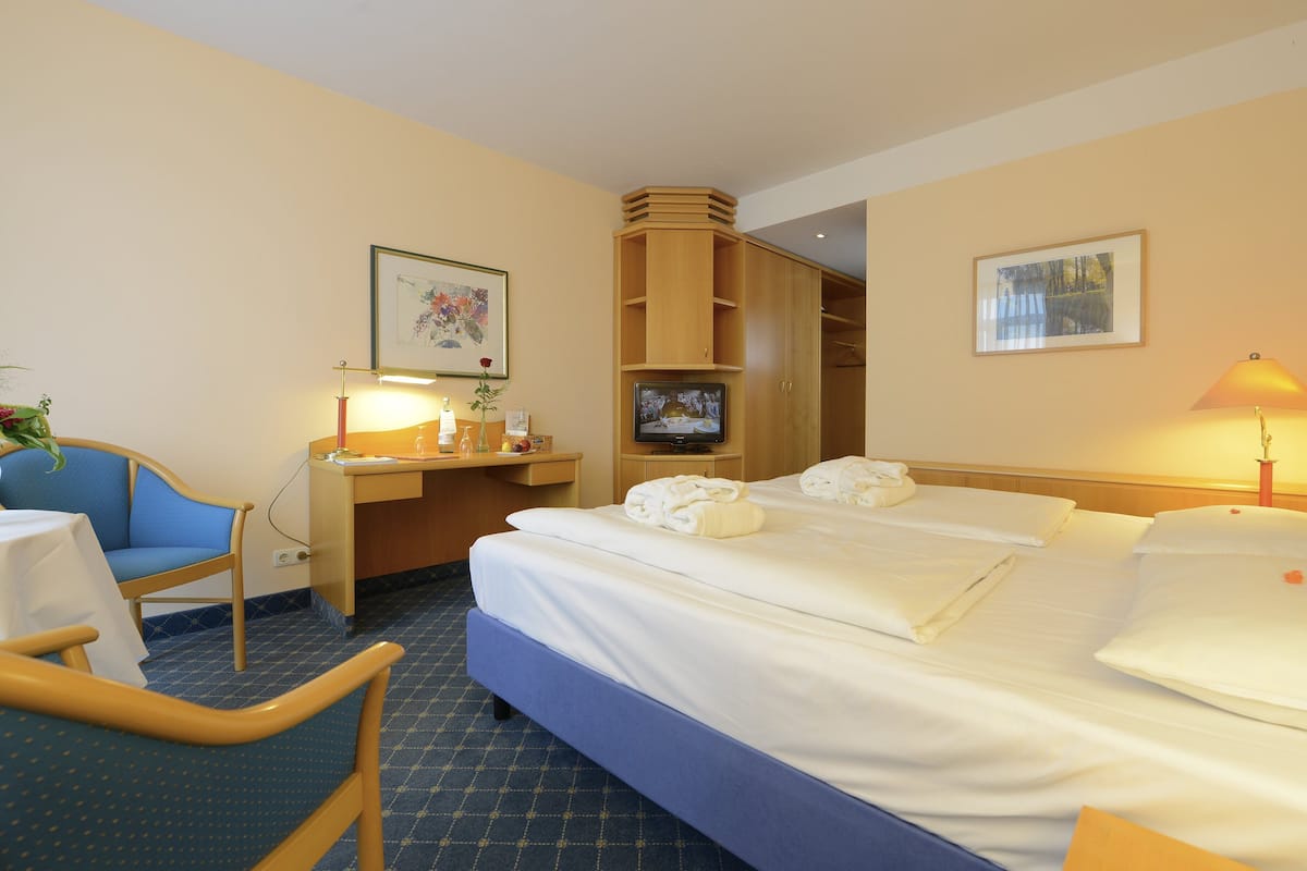 A hotel room with a bed, a desk, a chair, a TV, and a lamp.