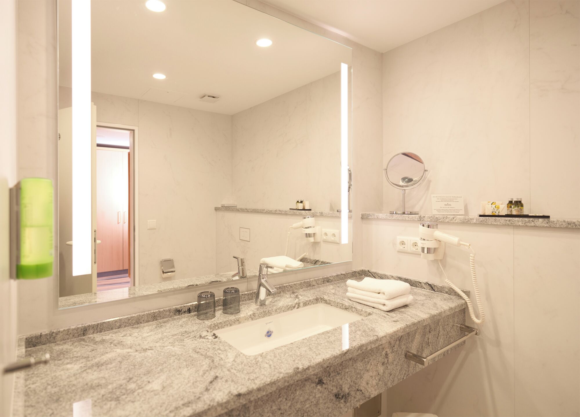 A modern bathroom with a marble sink, a large mirror, a hairdryer, and a towel rack.