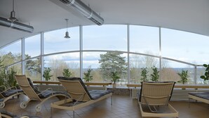 A sunroom with large windows, wicker lounge chairs, and potted plants. - TOP CountryLine Seehotel Großherzog Ostseebad Boltenhagen (Boltenhagen)