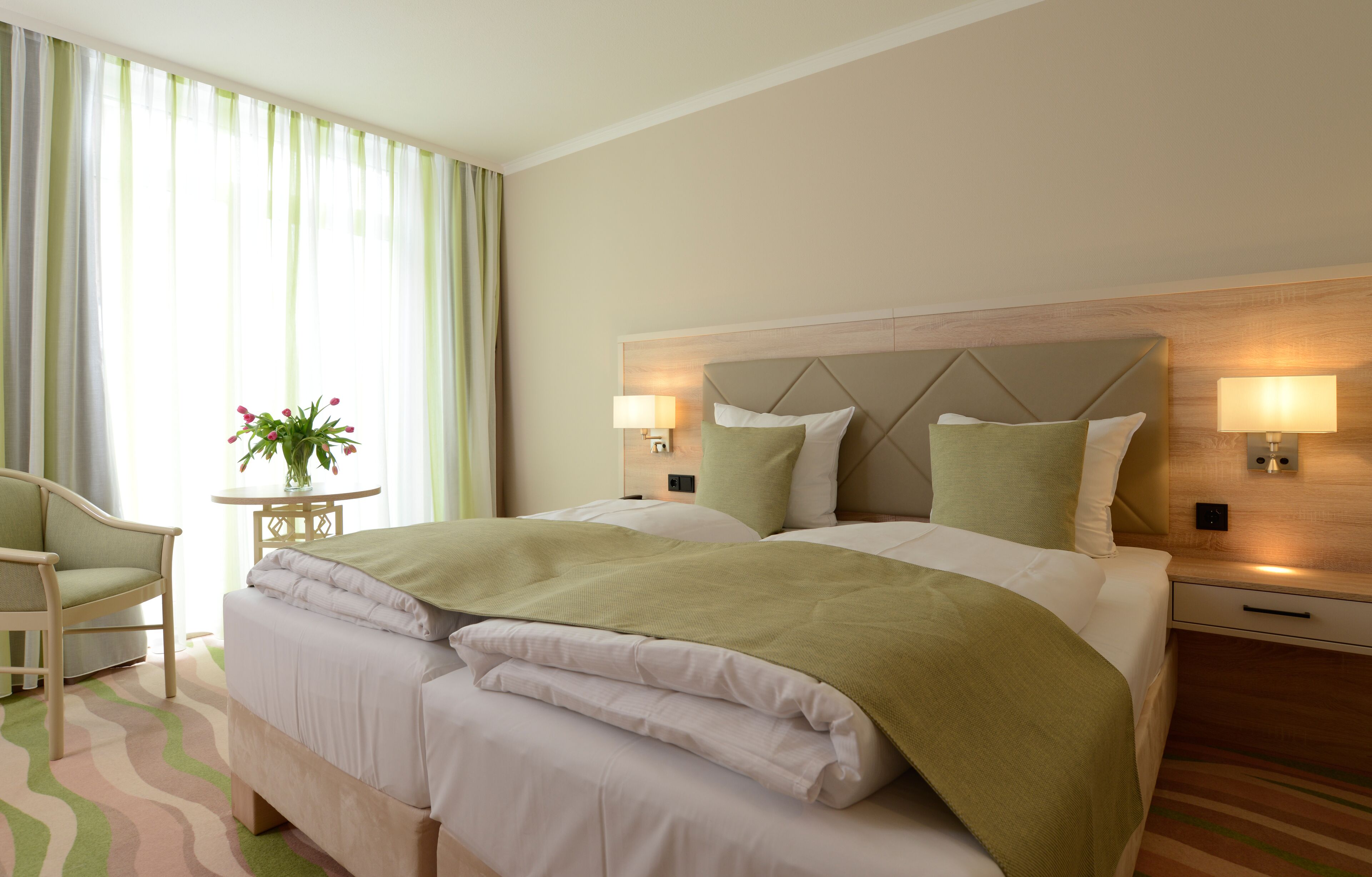 Een hotelkamer met een bed, een stoel, een tafeltje met een plant en twee wandlampen.