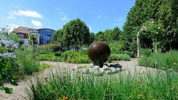 A garden with a spherical water feature, surrounded by greenery and a building in the background.