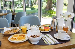 Una mesa de desayuno con diversas opciones de comida, como panqueques, un tazón de cereal, fruta fresca y una taza de té.
