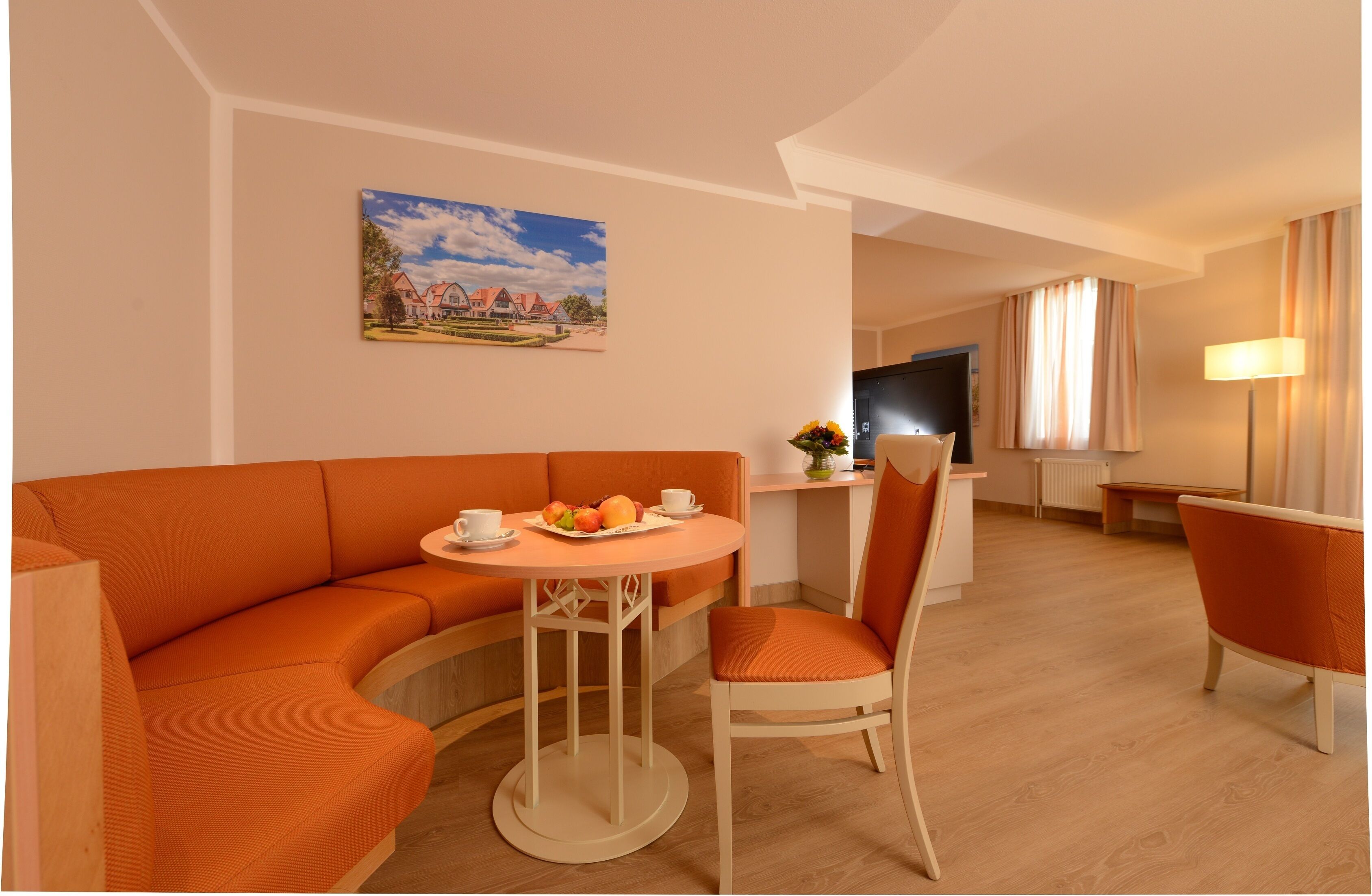 Une chambre d’hôtel moderne avec un canapé orange aux lignes courbes, une table ronde sur laquelle sont disposés des fruits, une télévision et une lampe.