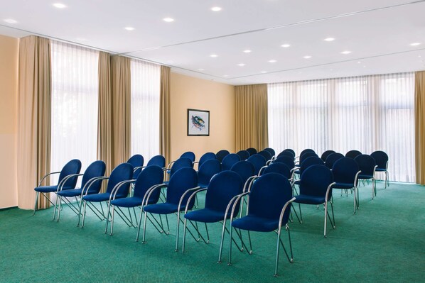 A conference room with rows of blue chairs, beige curtains, and a green carpet.