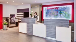 Una recepción de hotel con diseño moderno, una gran pantalla digital con un mapa y una planta en maceta.