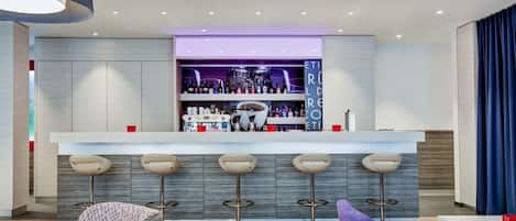 Una zona de bar moderna con una barra central, varios taburetes y un área de estar con sofá y sillones.