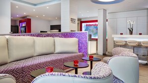 Un moderno vestíbulo de hotel con zona de estar, mostrador de recepción y bar.
