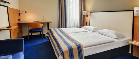 A hotel room with a bed, a desk, a chair, and a large window with curtains.