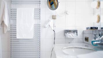 Een moderne badkamer met een witte handdoekhouder, een ronde spiegel, een losse haardroger, een handdoekdispenser en een wastafel met een kraan.