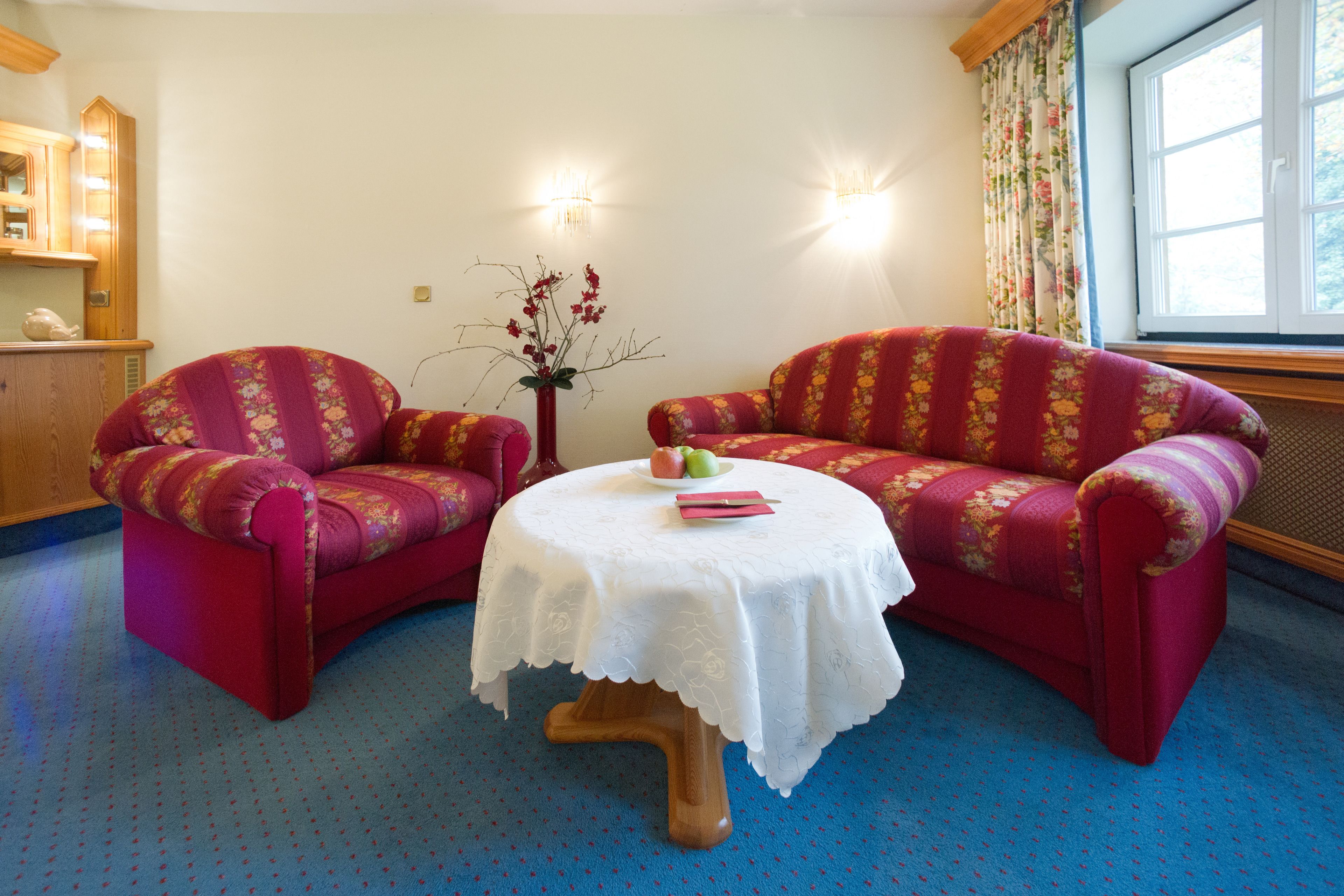 A room with two red upholstered sofas, a small round table with a white tablecloth, and a vase with flowers.