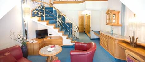 A living room with a red leather sofa, a small round table, a television, and a staircase leading to an upper level.
