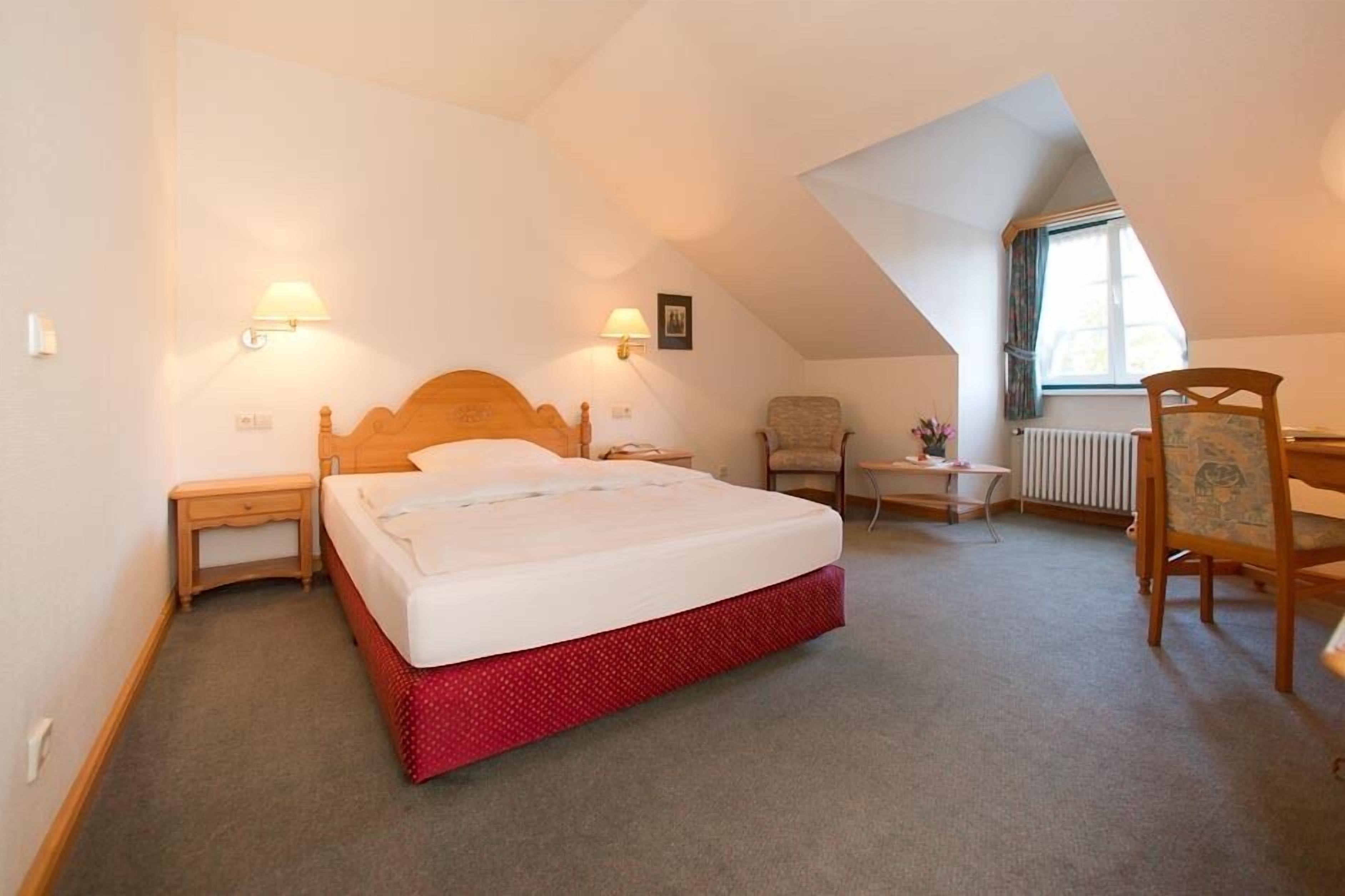 A bedroom with a bed, two bedside tables, a chair, a small table, and a radiator.