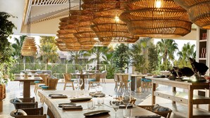 A restaurant with wicker chandeliers, wooden tables, and chairs, overlooking a tropical garden. - Porto Sani (Kassandra)
