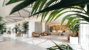 A spacious lobby with a high ceiling, modern furniture, and abundant indoor plants. - Porto Sani (Kassandra)