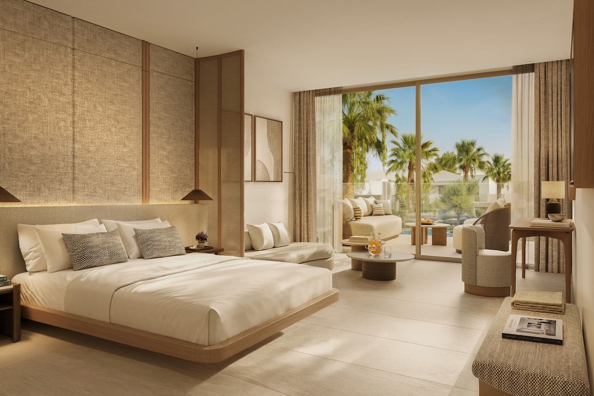 A modern hotel room with a large bed, a seating area with a view, and a balcony with palm trees.