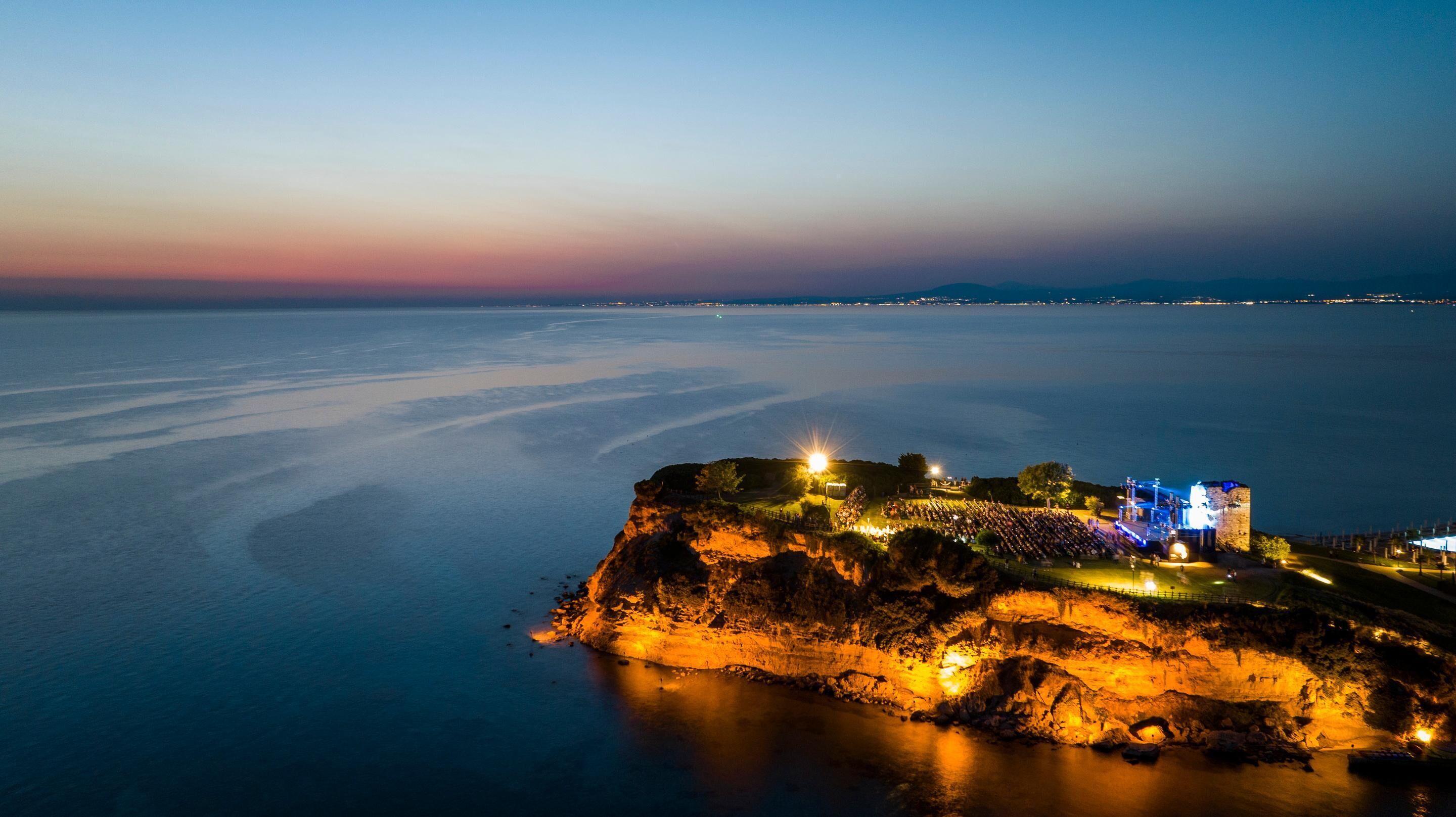 A coastal fortification with a viewing platform, illuminated by artificial lighting, overlooking a calm sea.
