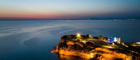 A coastal fortification with a viewing platform, illuminated by artificial lighting, overlooking a calm sea.