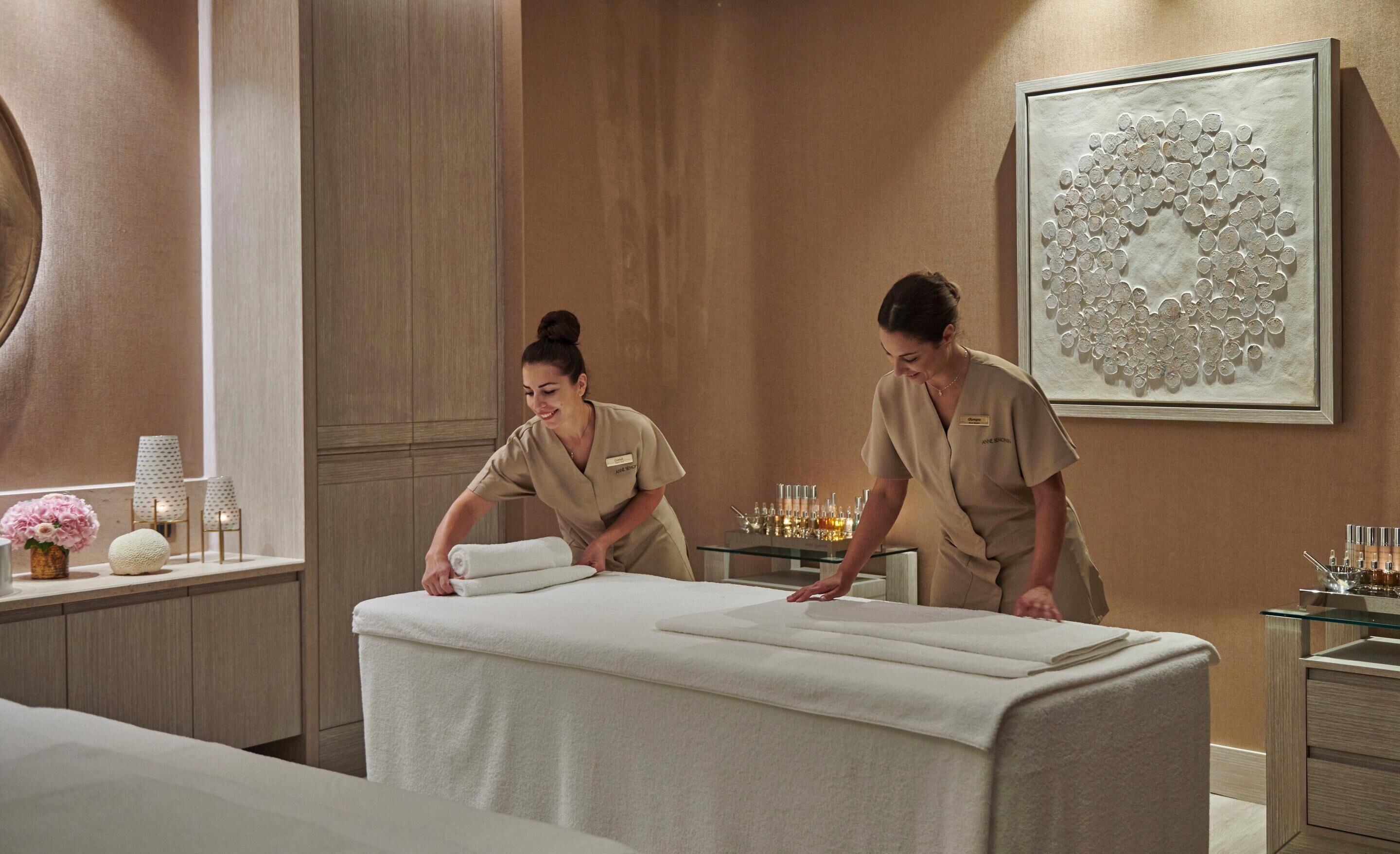 Een spa ruimte met een massagetafel, een glazen vitrine met toiletartikelen en een decoratief wandkunstwerk.