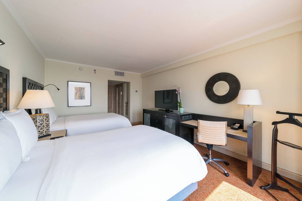 A hotel room with two beds, a desk with a computer, a TV, and a chair.