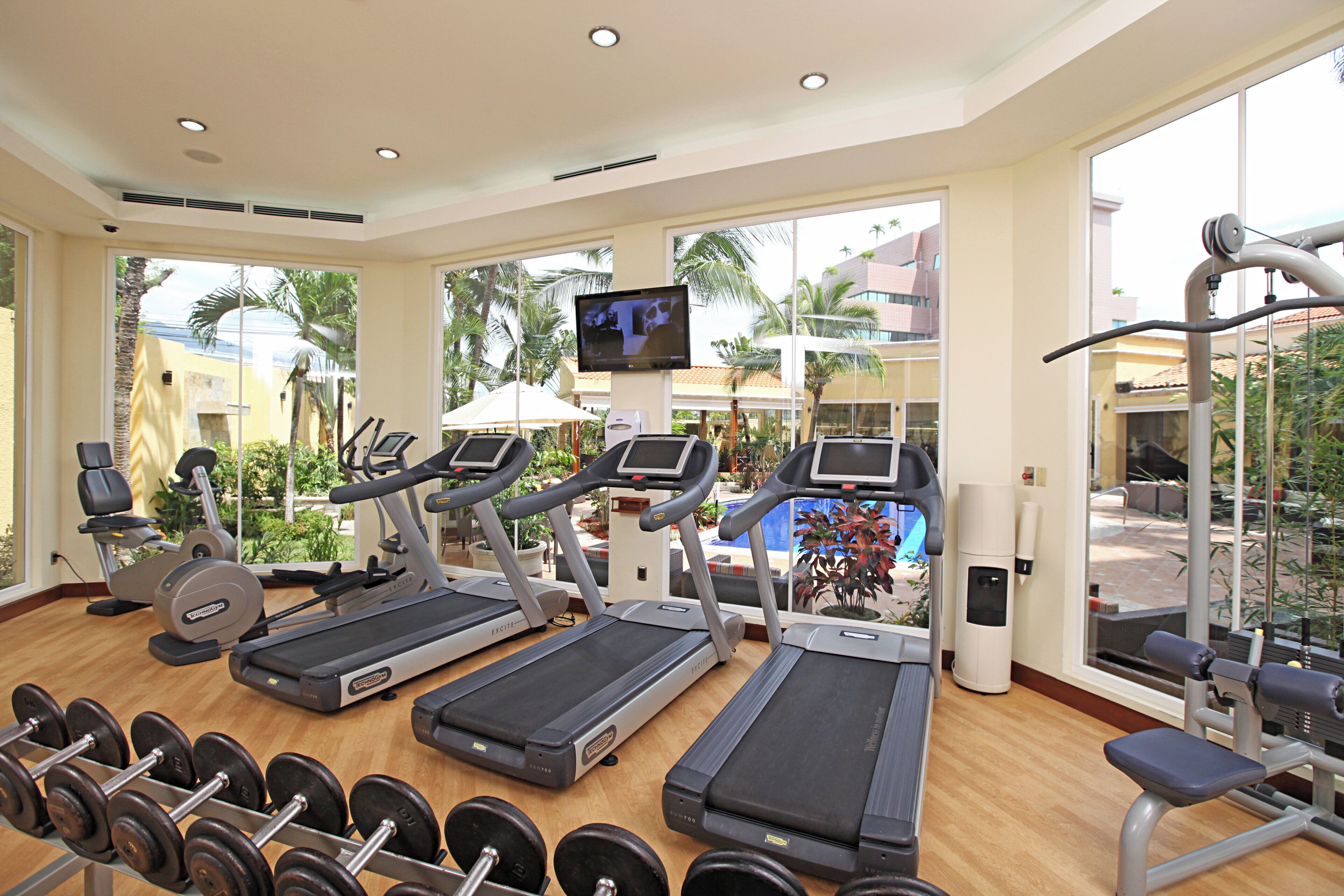 Un gimnasio con cintas de correr, mancuernas y una pantalla de televisión.