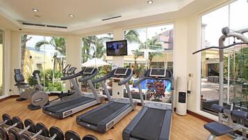 Un gimnasio con cintas de correr, mancuernas y una pantalla de televisión.