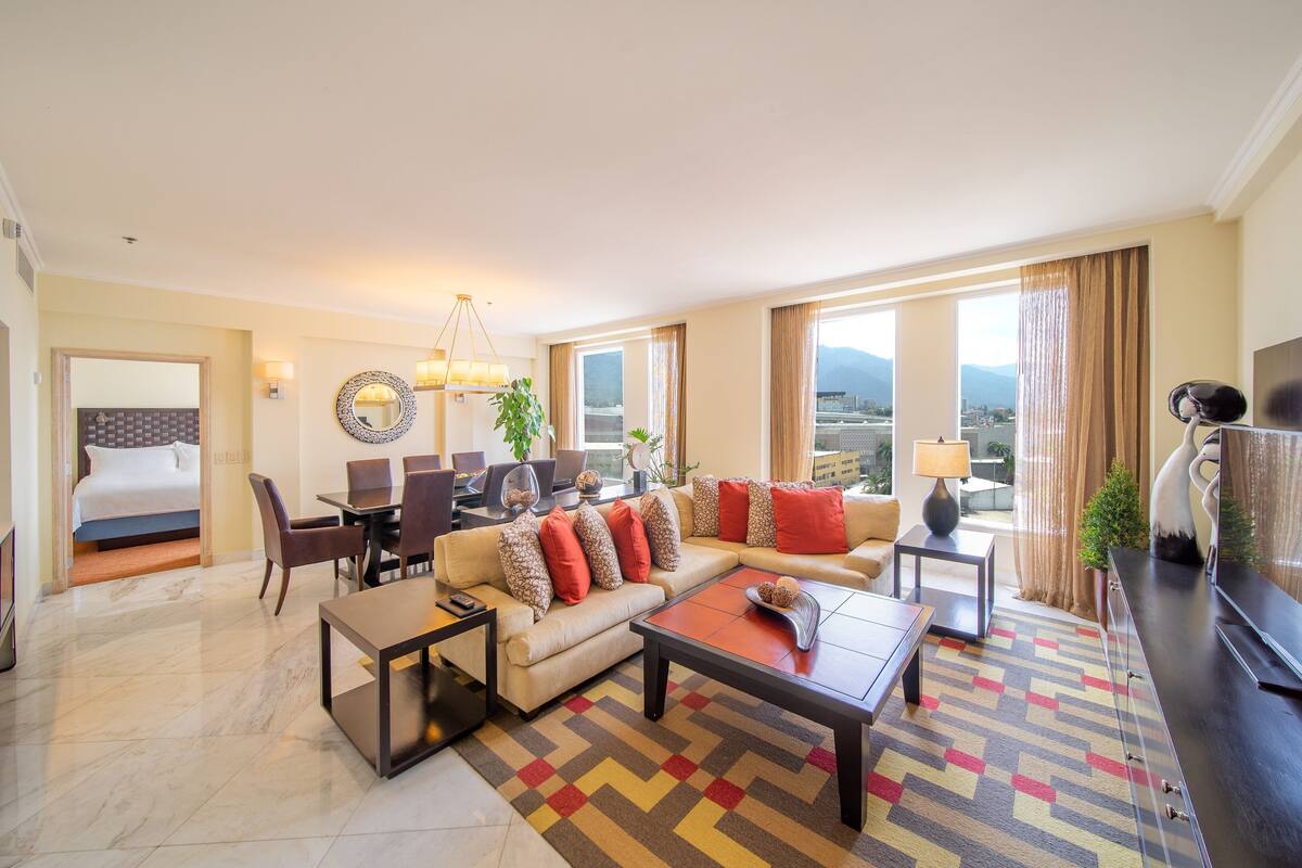 A hotel room with a bed, a sofa, a coffee table, a desk, and a TV.