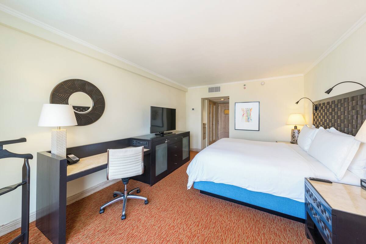 Une chambre d’hôtel équipée d’un lit, d’un bureau, d’une chaise, d’une télévision et d’un miroir fixé au mur.