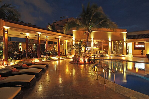 Zona de piscina con sillones reclinables, una piscina y un restaurante.