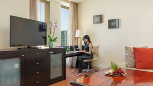 Une chambre d’hôtel équipée d’une télévision, d’un bureau, d’un ordinateur portable et d’une table à manger avec des fruits.