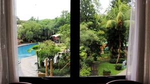 A view from a window overlooking a swimming pool and lush greenery, including palm trees and various plants. - Prime Plaza Hotel - Purwakarta (Cikampek)
