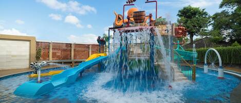 Un parque acuático con un tobogán azul grande, una fuente de agua y una estructura de juego con figuras de animales.
