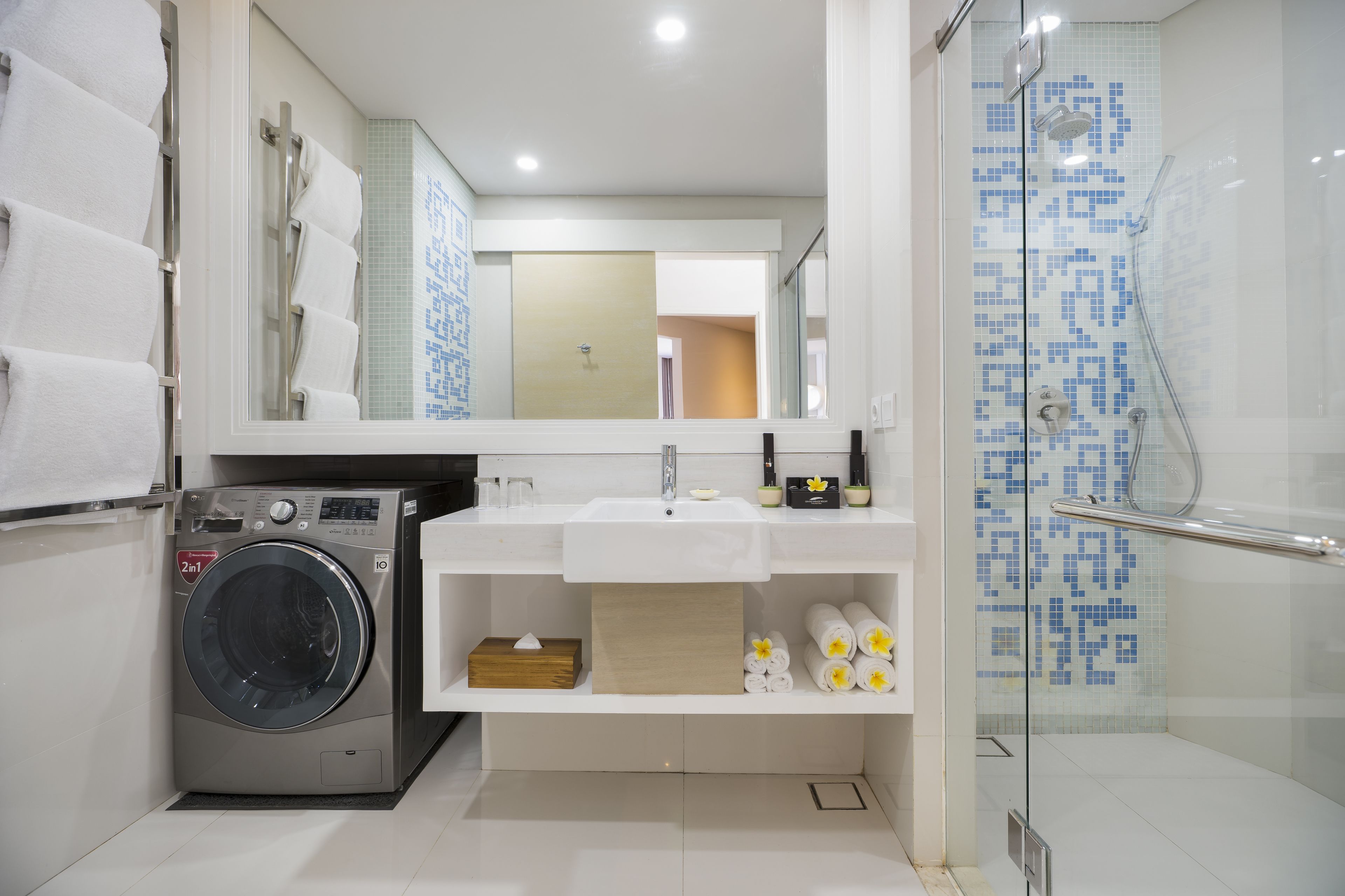 A modern bathroom with a washing machine, a sink with a mirror above, and a glass shower enclosure.