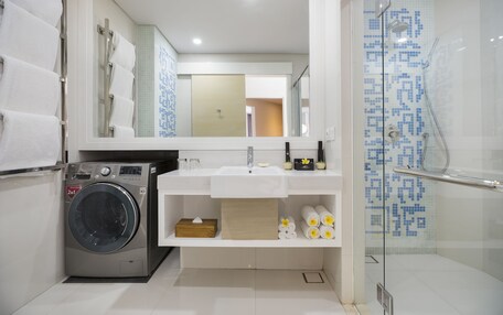A modern bathroom with a washing machine, a sink with a mirror above, and a glass shower enclosure.