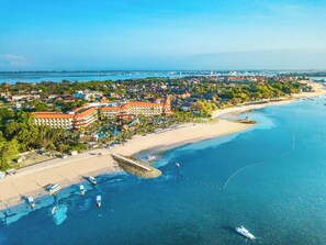Eine Vogelperspektive eines Küstenresorts mit Strand, klarem blauen Wasser und einem großen Hotelkomplex.