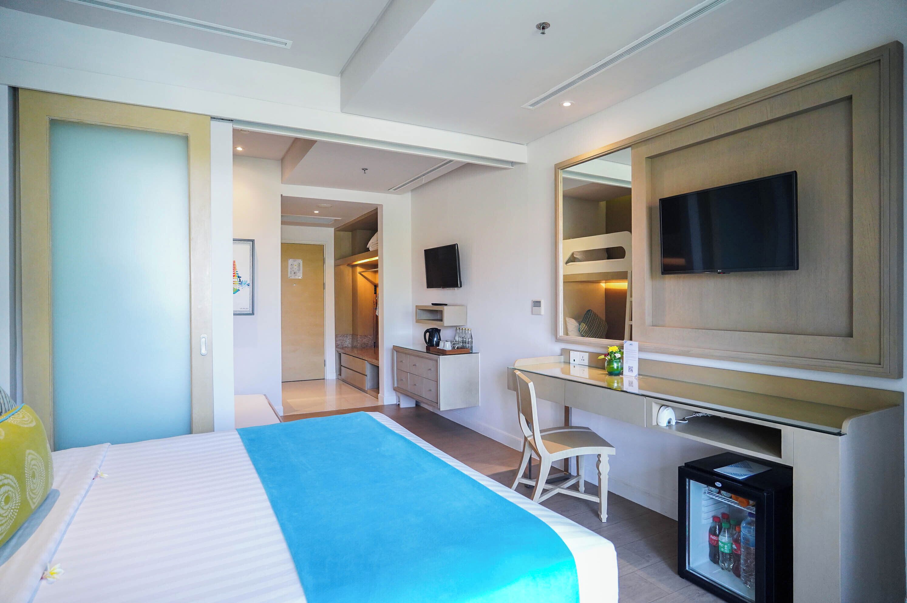 A hotel room with a bed, a desk, a chair, a television, and a minibar.