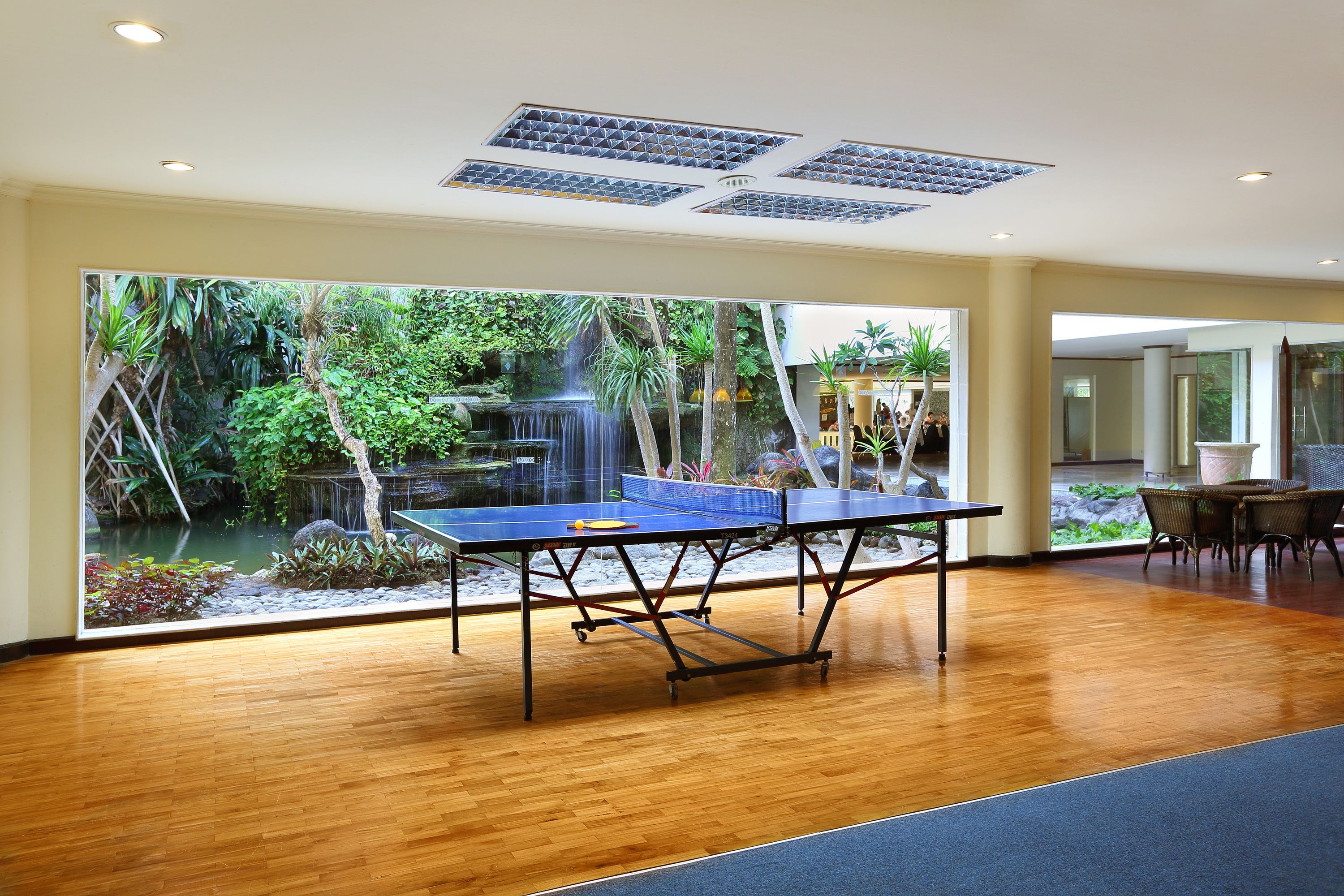 Una sala con un tavolo da ping pong e un'ampia finestra che si affaccia su un giardino con una cascata.