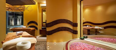A spa room with a massage table, a large mirror, and a flower-filled water feature.
