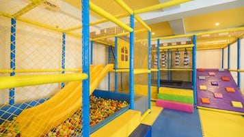 Un área de juegos interior con piscina de pelotas, tobogán y estructuras de juego acolchadas.