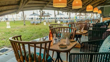An outdoor dining area with wooden tables and chairs, umbrellas, and hanging lights.